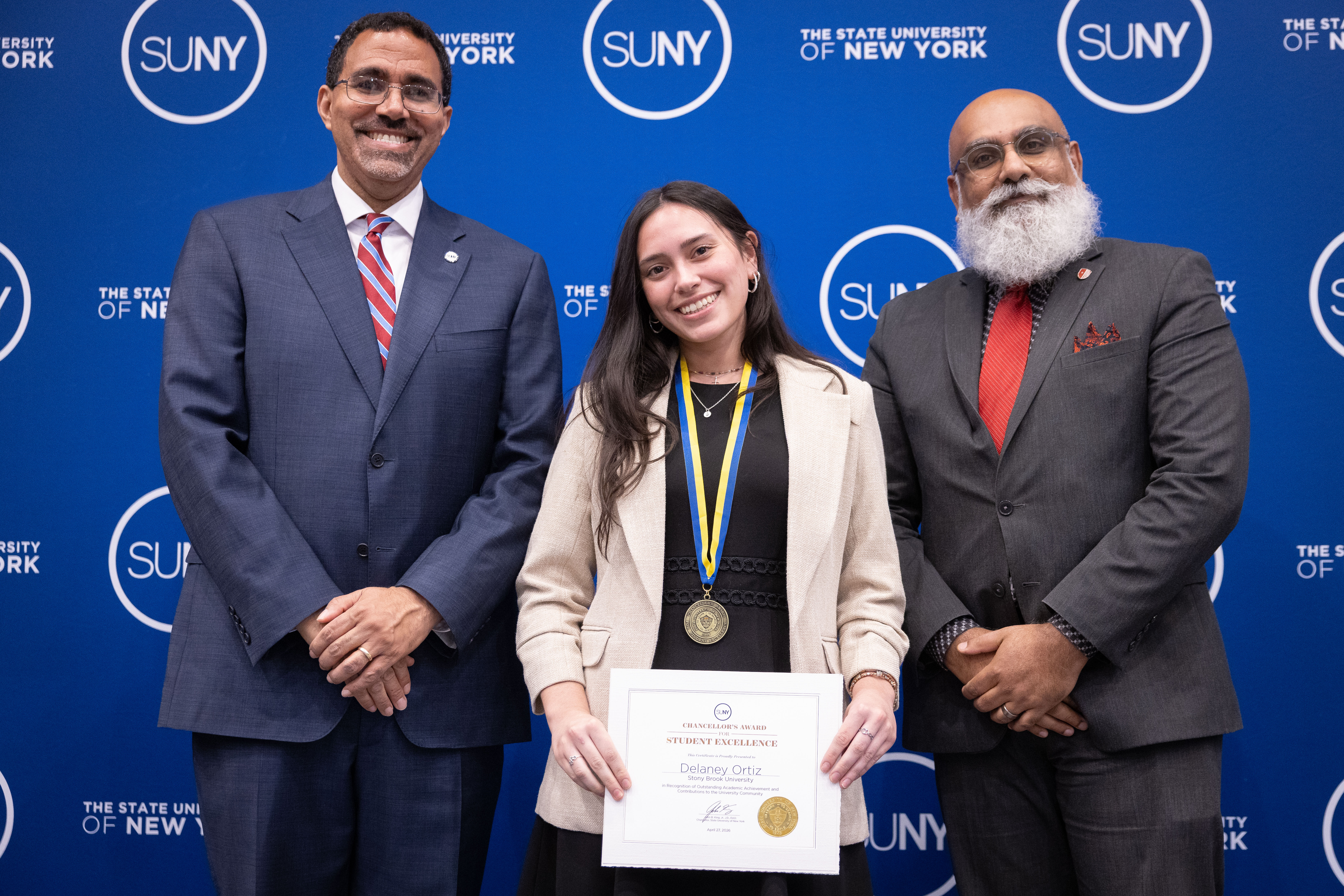Three people standing for a photo; Delaney Ortiz in the middle holding a certificate. 